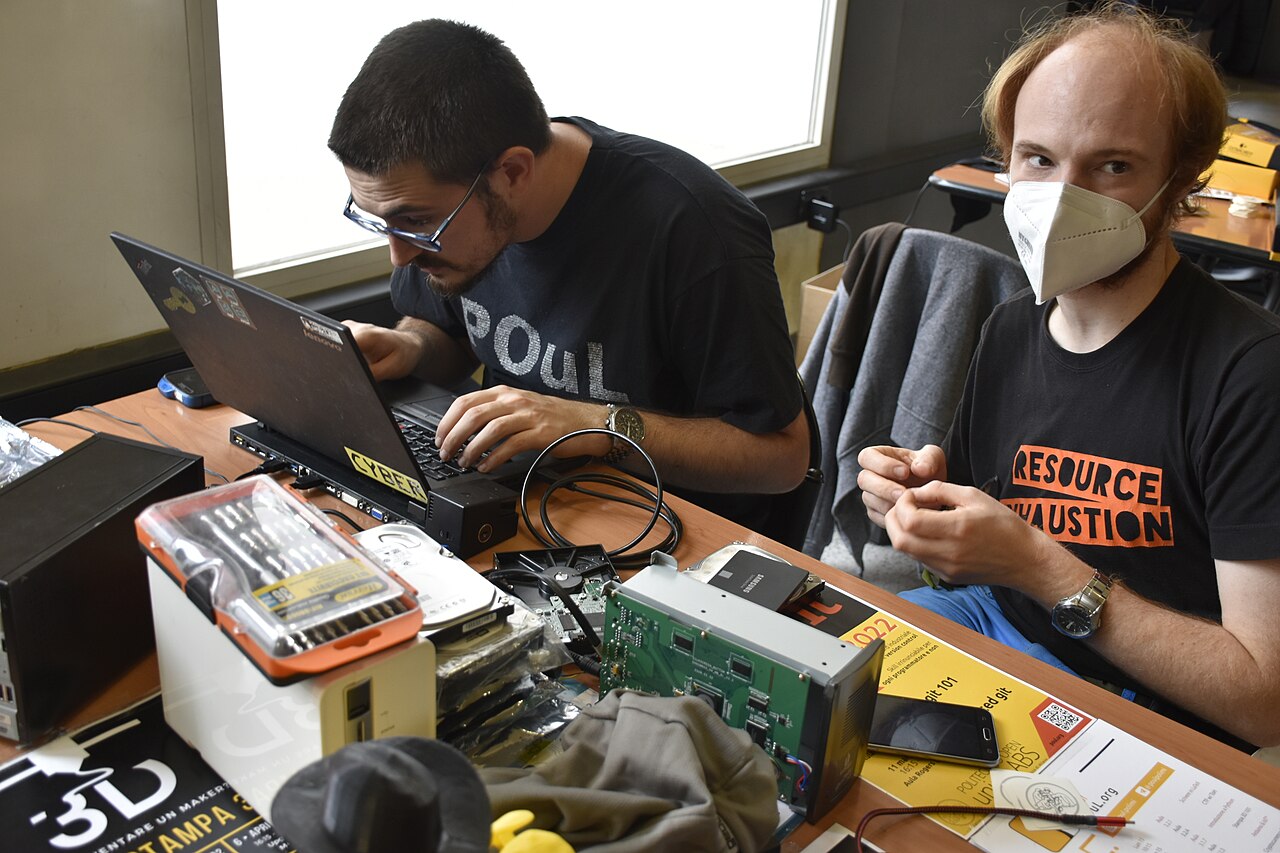 The Symlink Hack That Turns Claude Code into an Headless API Backend for OpenClaw — Hackers working on Linux laptop with computer disks and repair kits - Milano 2022
